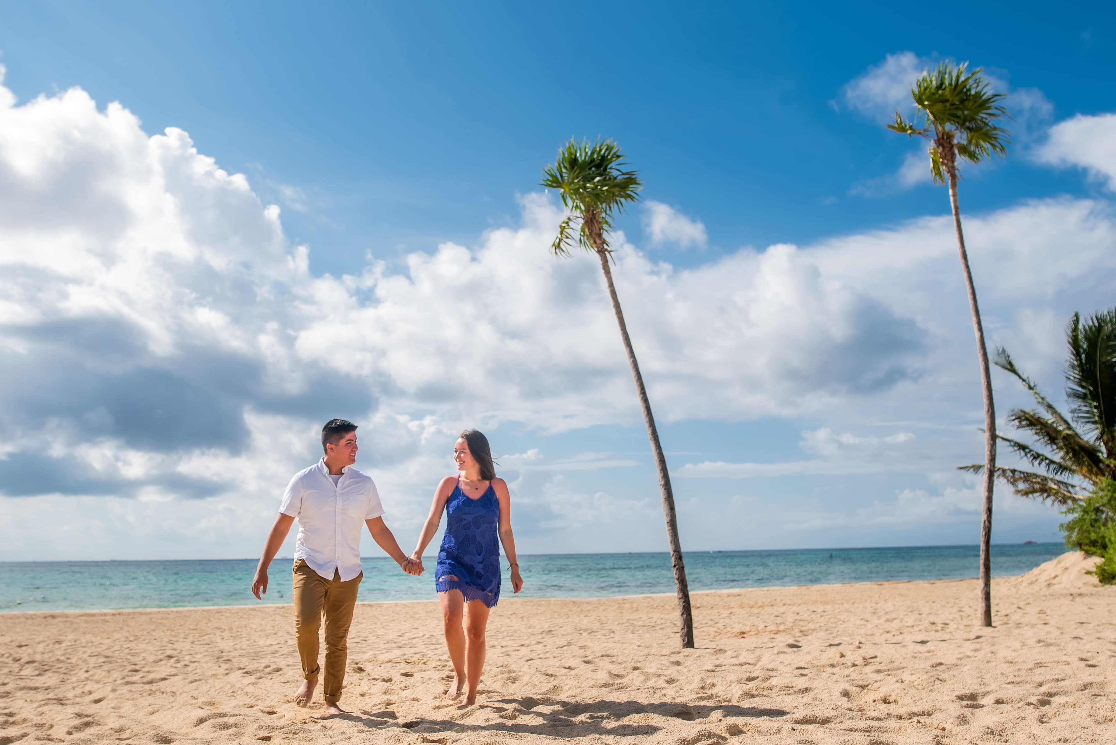 Eli and Hannah walking on the beach near palm trees.