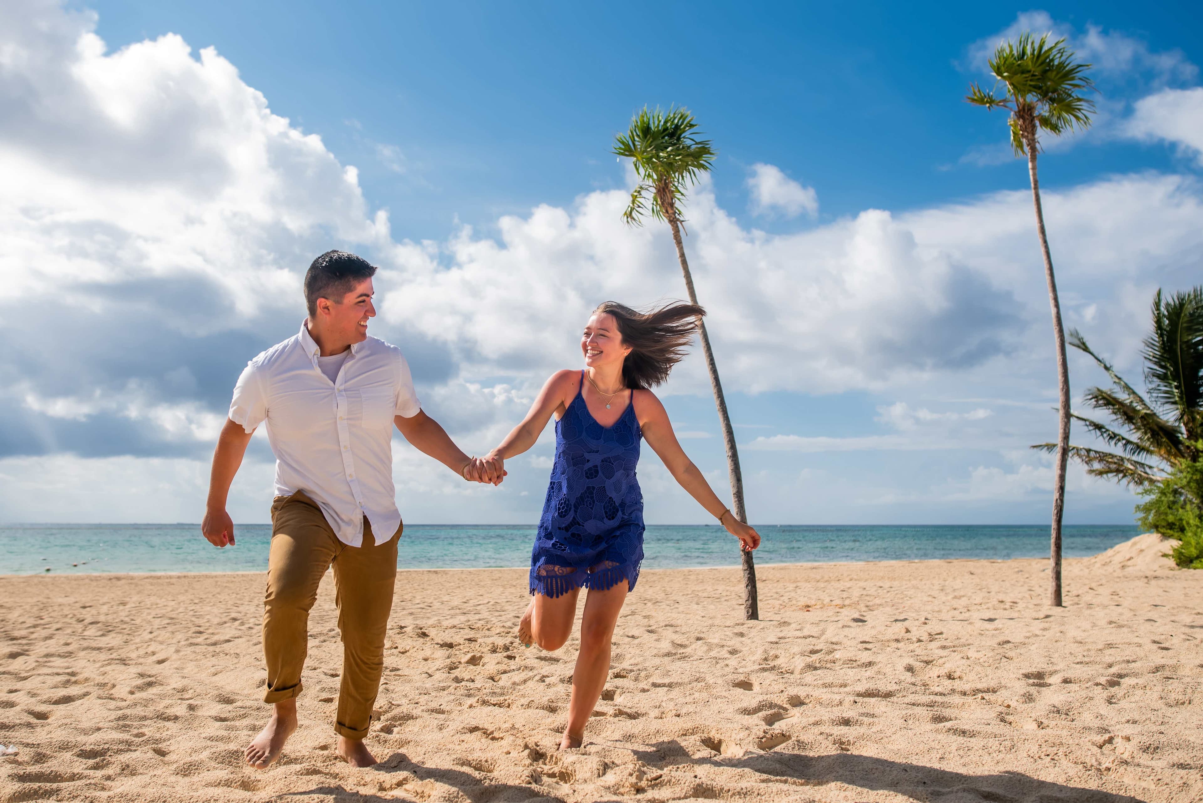 Eli and Hannah running on the beach near palm trees.