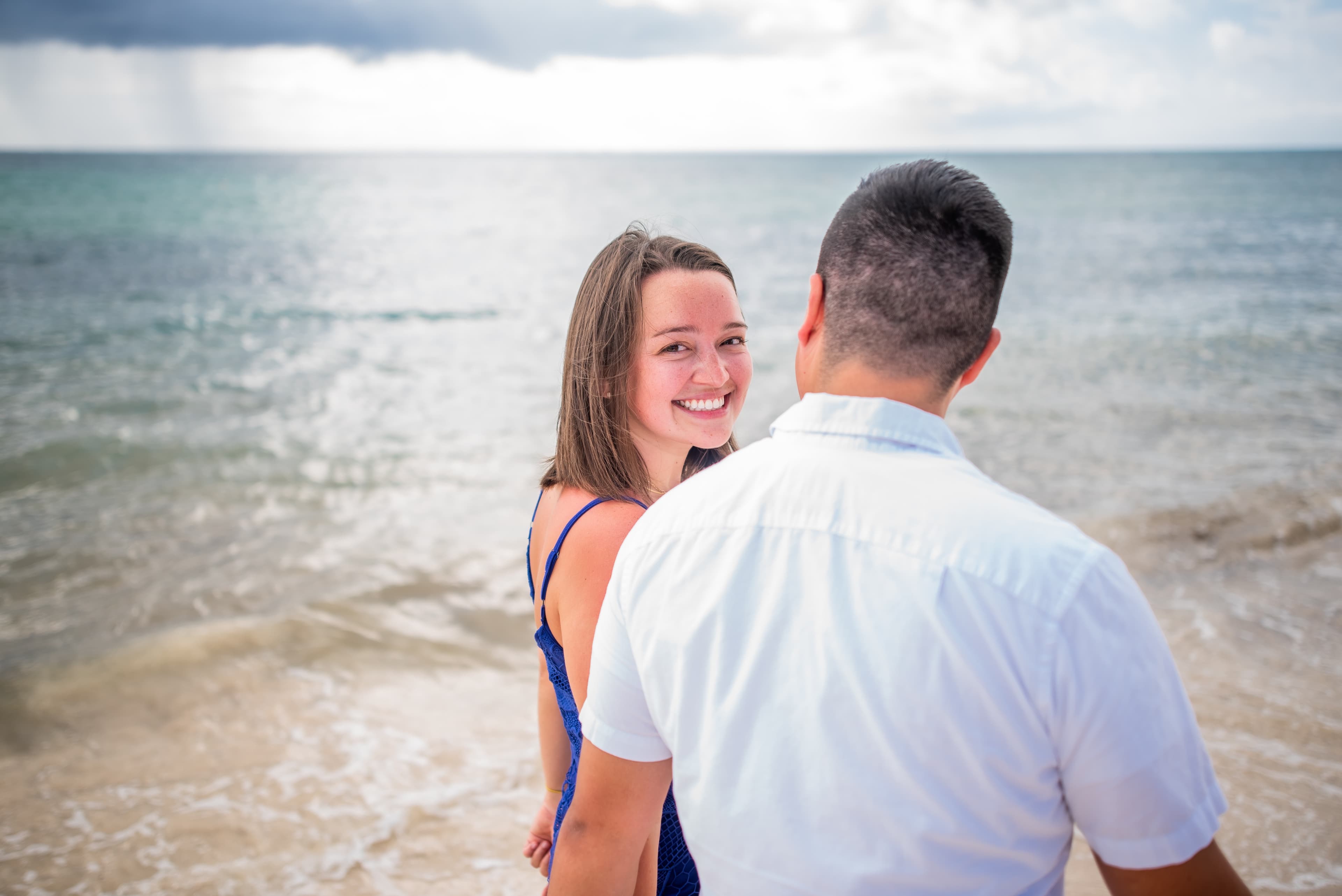 Hannah smiling over Eli's shoulder with the ocean behind her.