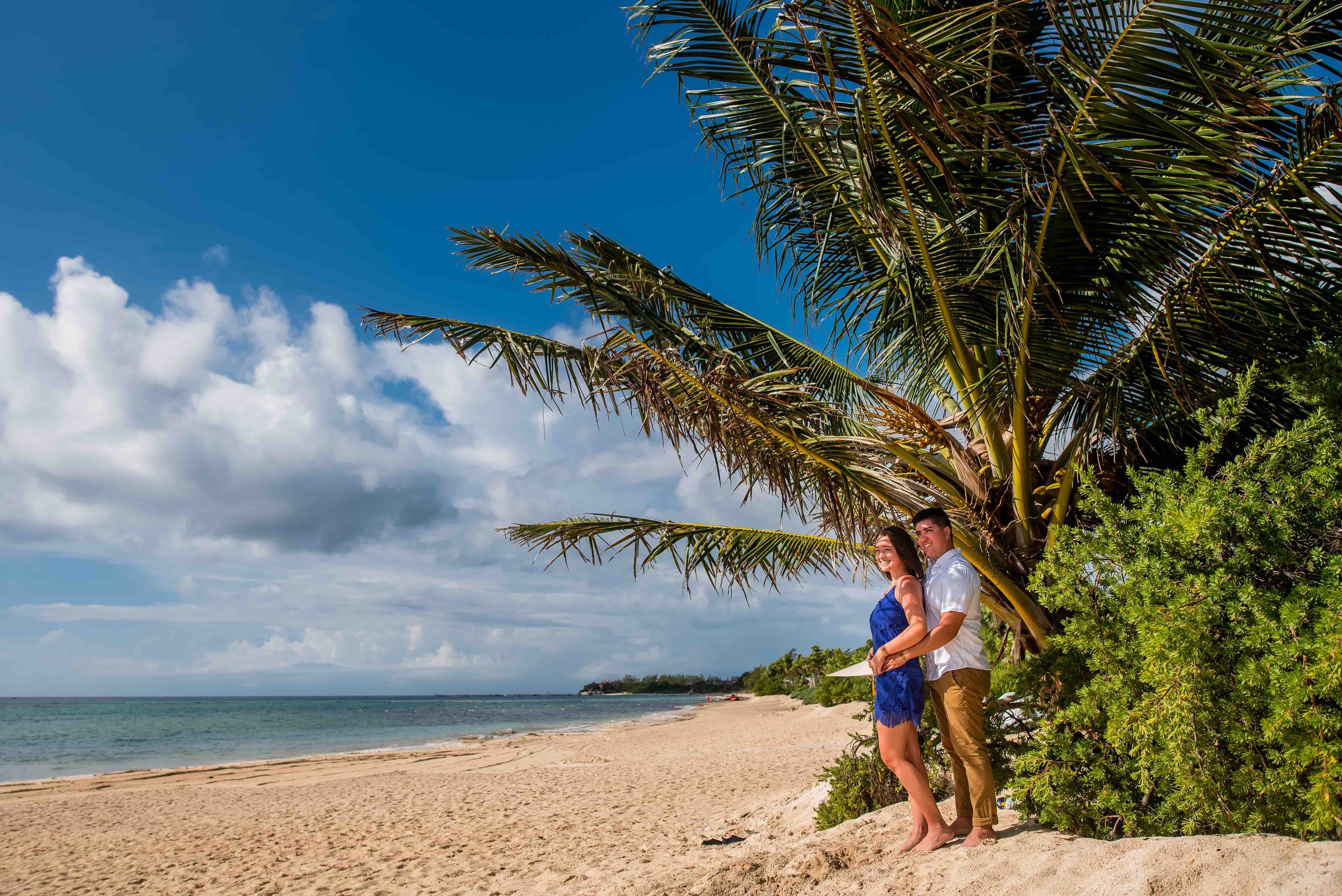 Eli and Hannah standing near greenery on the beach.